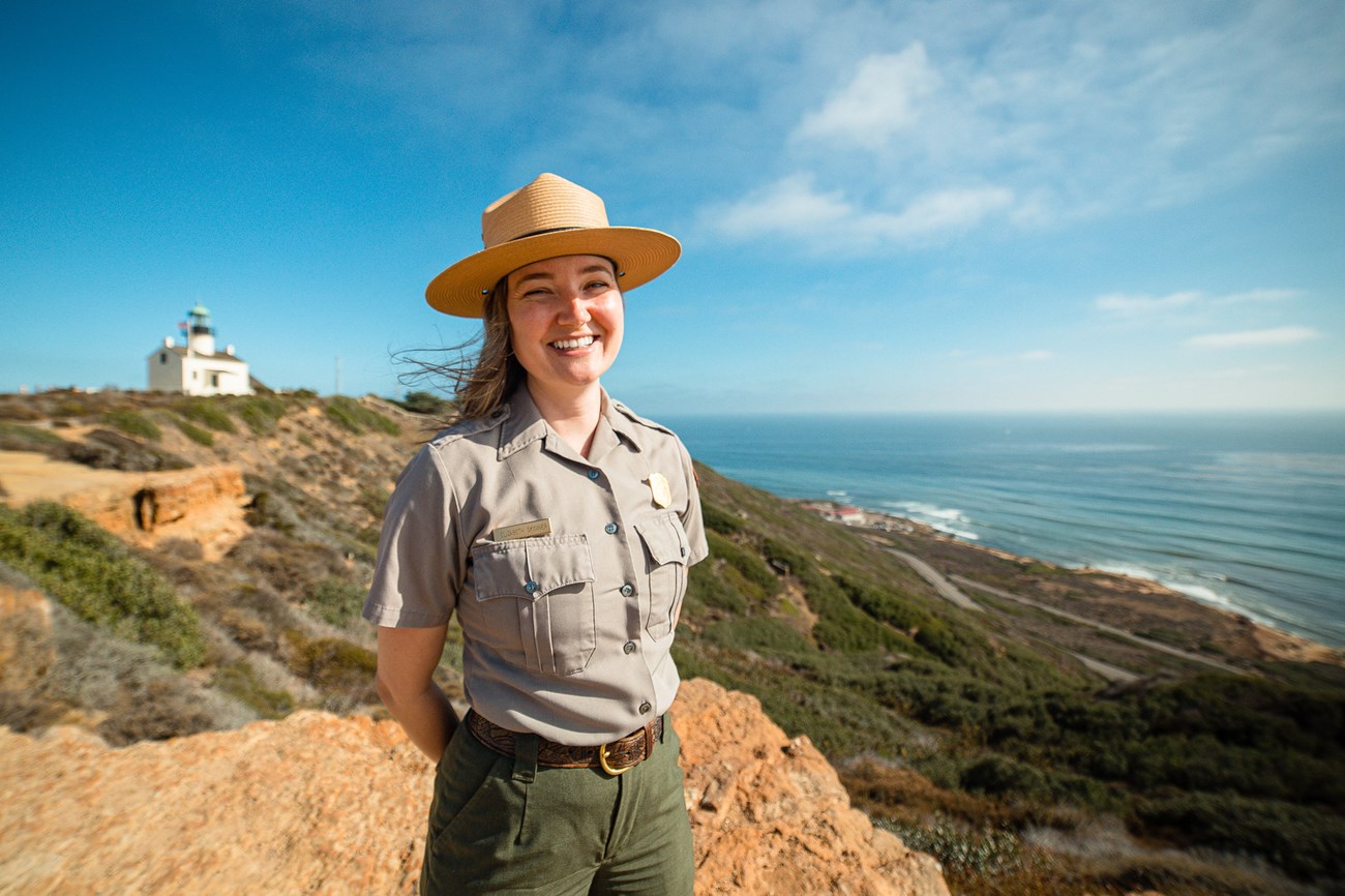 A smiling female park ranger with a lighthouse in the background