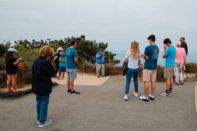 Park Volunteer talks to a group of people in front of a low rock wall