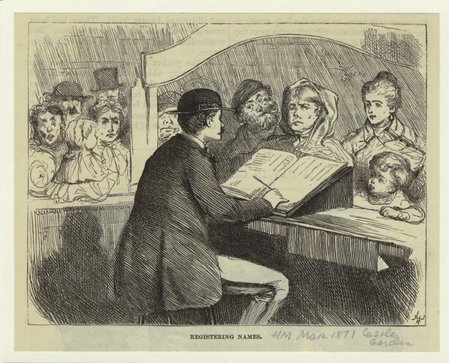 A man writing in a book on a desk with a crowd of people in front of him.