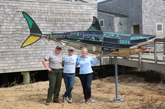 Three people pose and smile by the back of a truck that is loaded with marine debris.