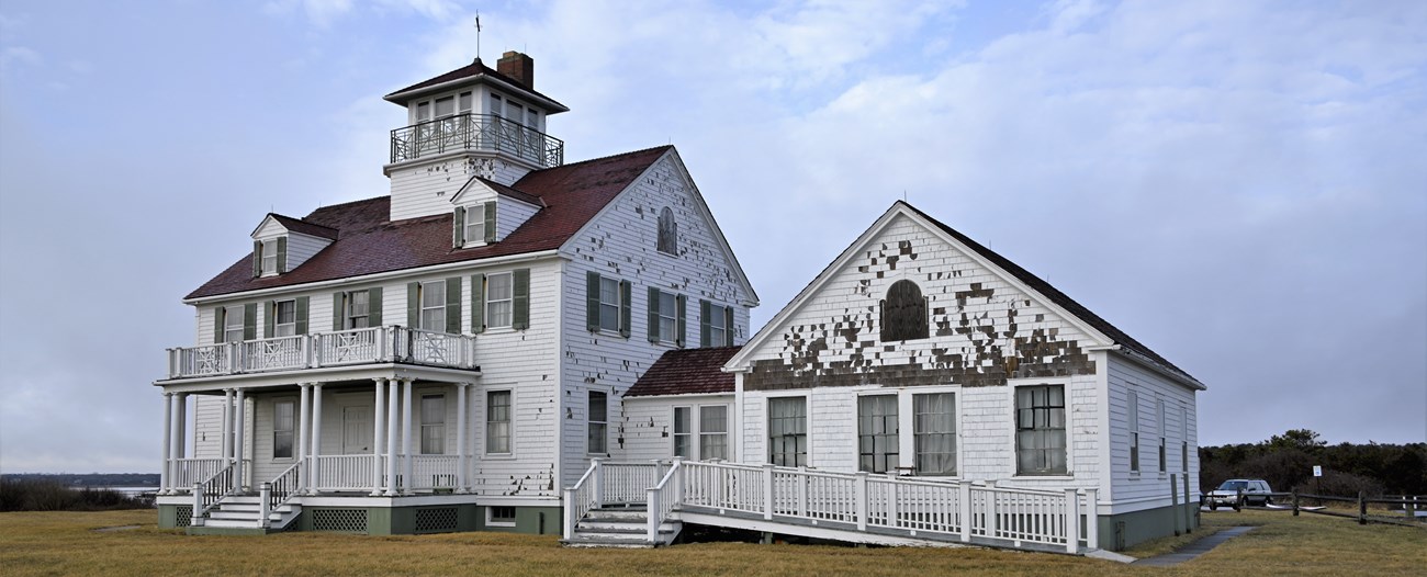A large three story building with significant damage to the white shingle siding.