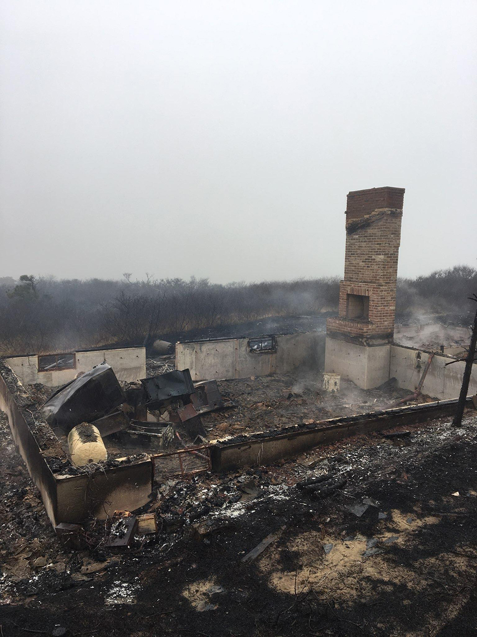 The smoldering remains of a house, all that is left is the scorched chimney and floor.