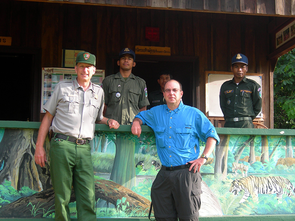 Two men stand in front of a forest themed kiosk. Two men are standing inside the kiosk.