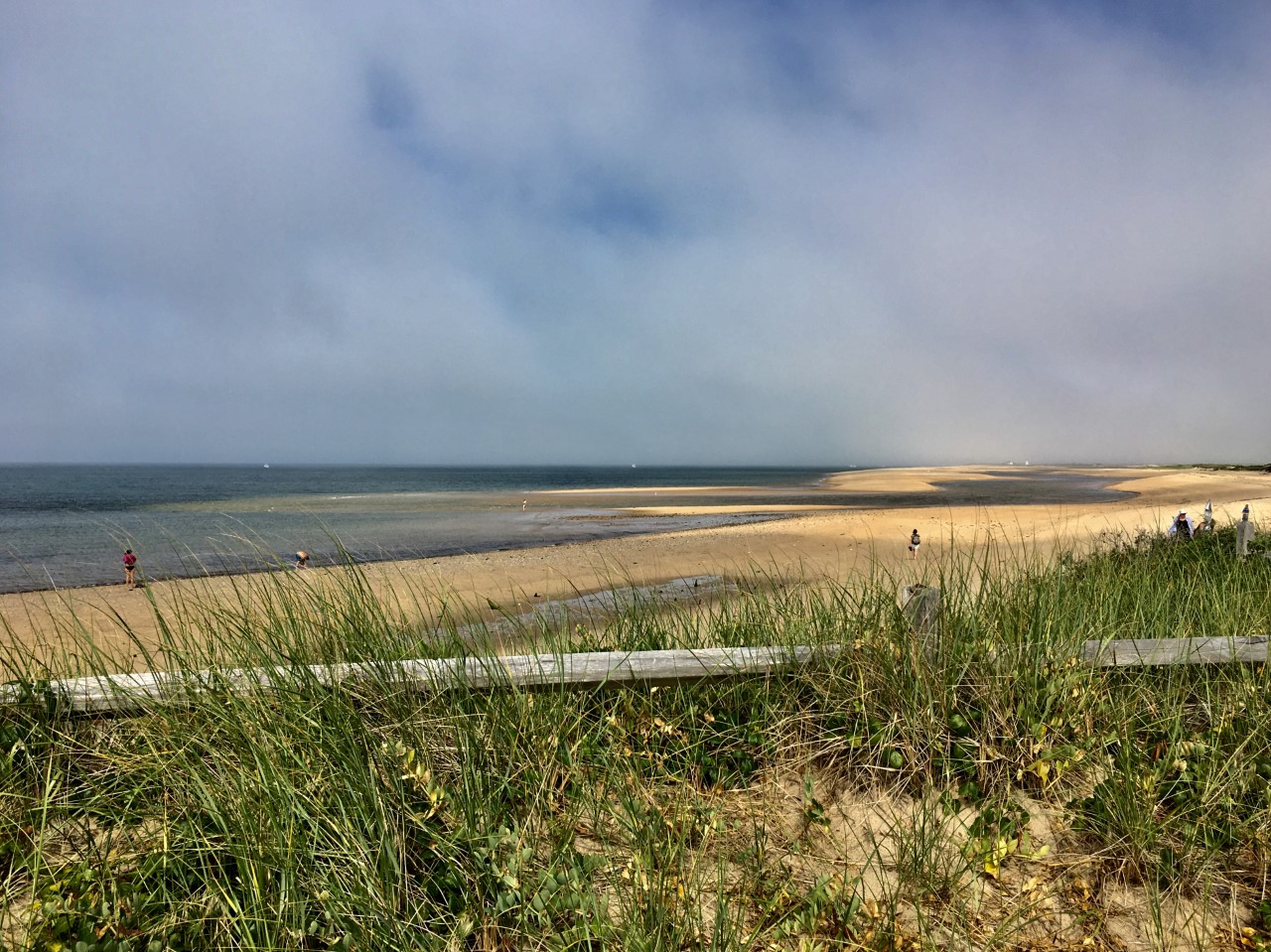 Long flat beach with tranquil water and faint outline of a lighthouse in the distance