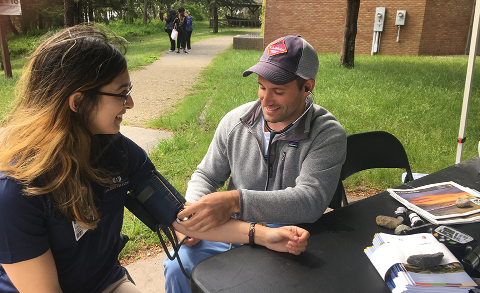 Healthy Parks, Healthy People blood pressure screening. A woman wearing glasses gets her blood pressure checked by a man wearing a ball cap.