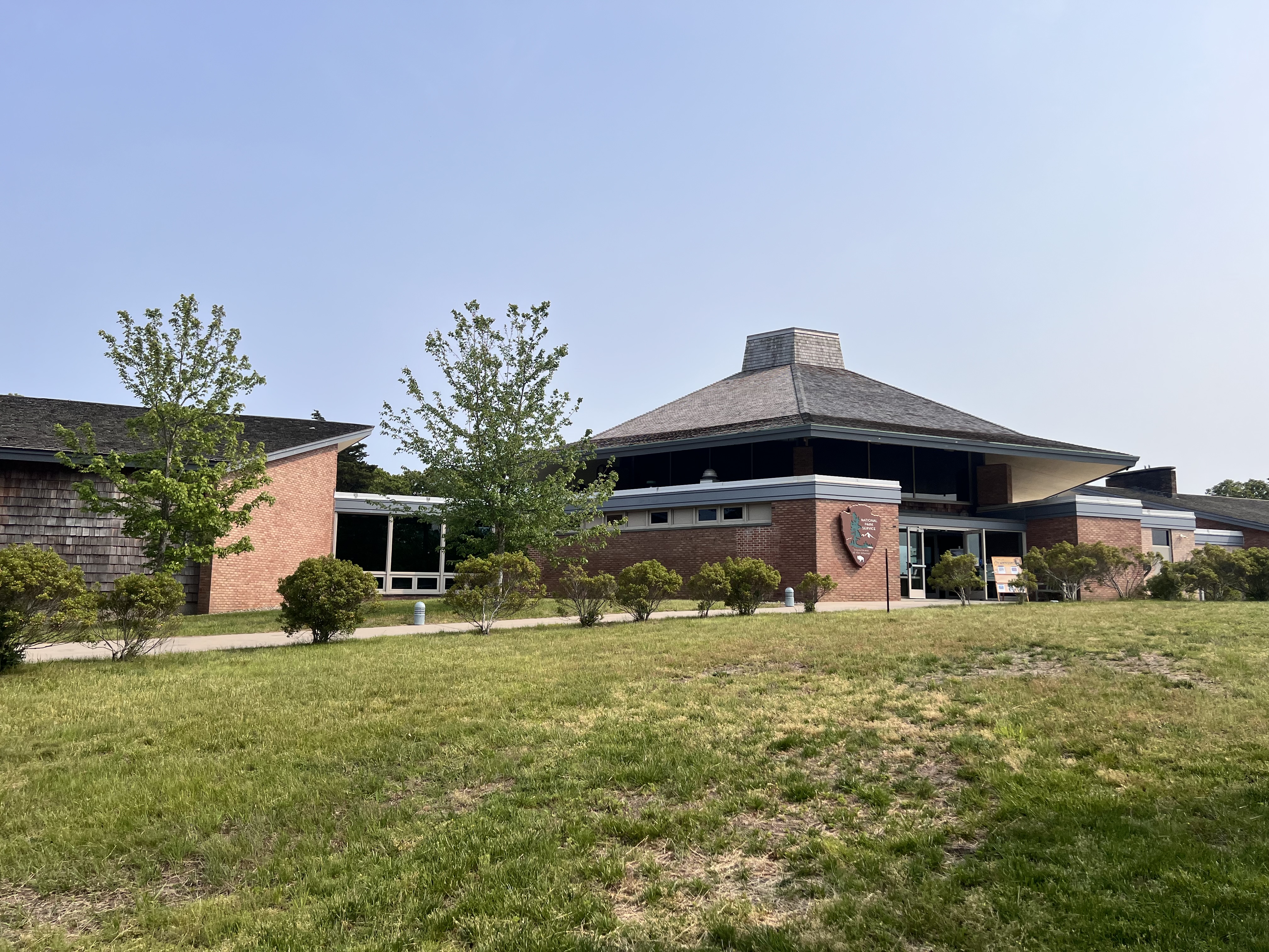 A brick and tan shingled visitor center with a green lawn and bushes.