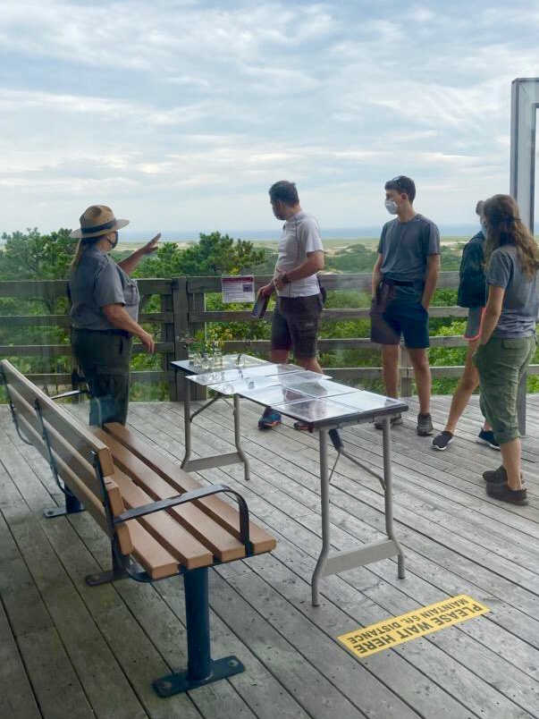 A park ranger stands on an outdoor deck talking with visitors
