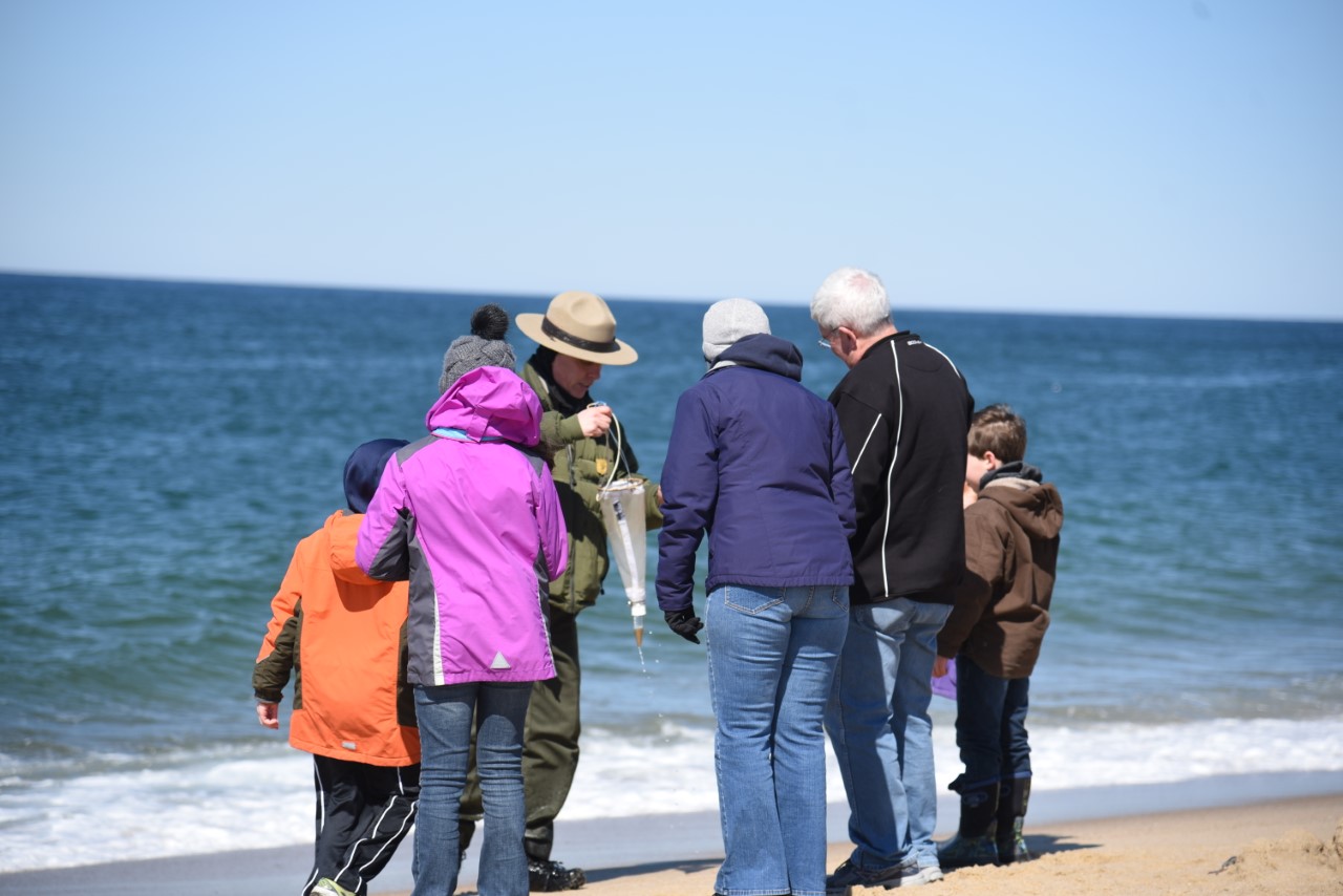 On a cold spring day a ranger stands on the beach with a group of visitors showing them an instrument that measures plankton