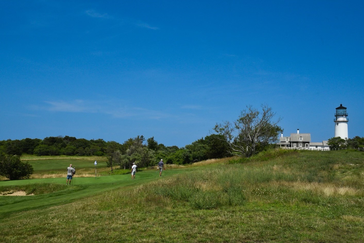 A group of golfers amongst green grass with a white lighthouse in the background.