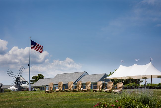 An American flag waves on the green hillside leading up to the Nauset Beach Inn. Adirondack chairs are set on the hillside overlooking the ocean.