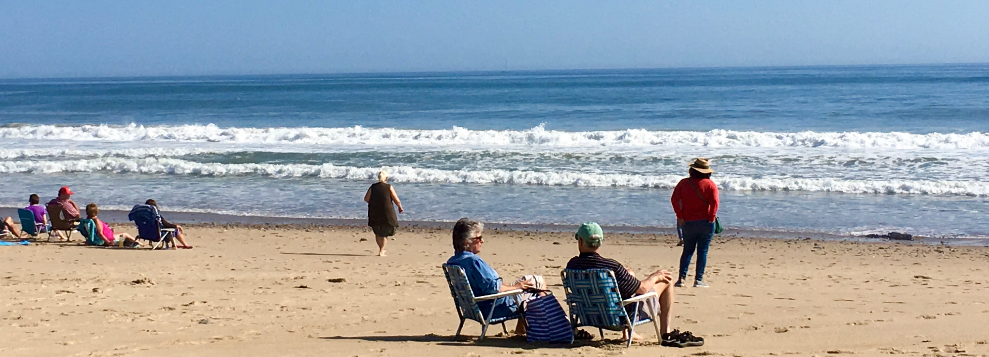 Several people stand and sit on chairs at the beach