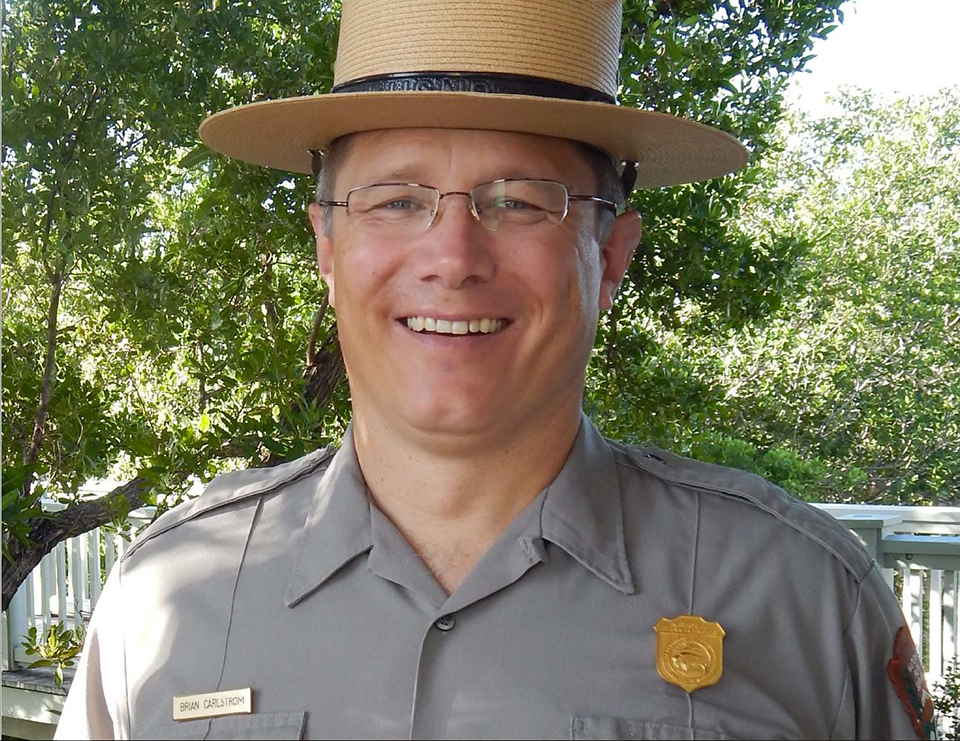 A man with round glasses, wearing a gray ranger uniform, and a wide, flat-brimmed hat.