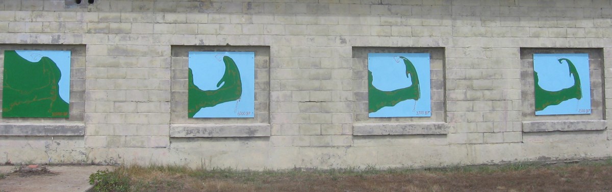 Coastal Change Four square murals on a brick wall, they are green and blue, and depict a land mass getting covered in water over time.