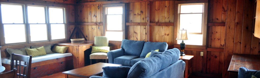 The inside of a rustic wood paneled cottage with large bright windows. The inside of a rustic wood paneled cottage with large bright windows.