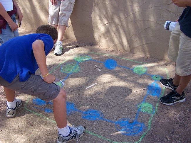 sidewalk chalk outlines the playing board for the 'stick game' students are learning