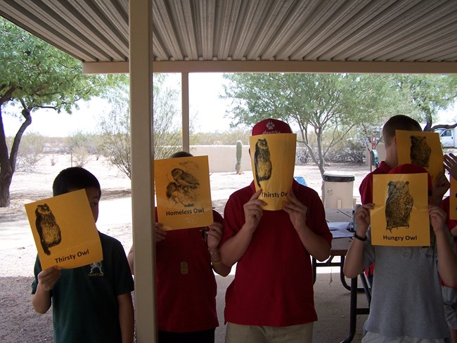 students cover their faces with gold cards explaining what resource they need (water, home, or food)