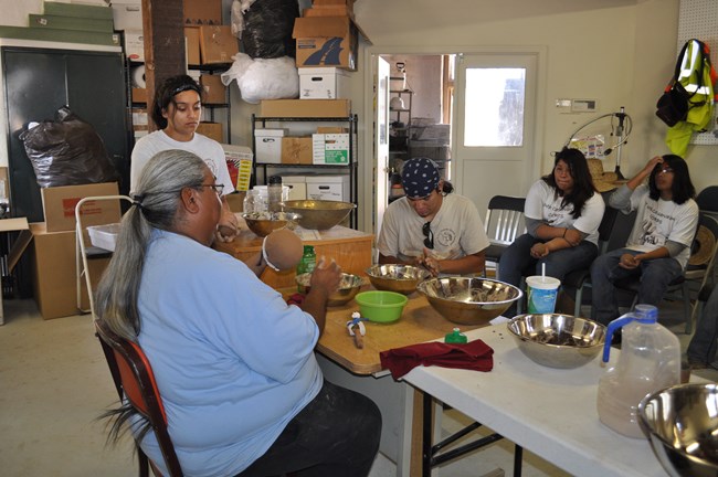 Ron Carlos sits in the foreground teaching student workers how to form clay pots with hands and simple tools