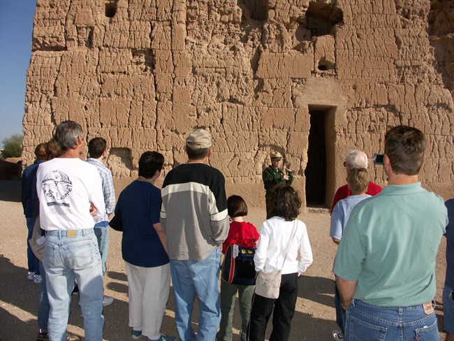 Ranger guiding tour group of families near the Great House. 11 people including children are listening to uniformed ranger.