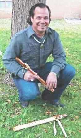 Tim Blueflint crouching in front of a tree to show off two of his flutes