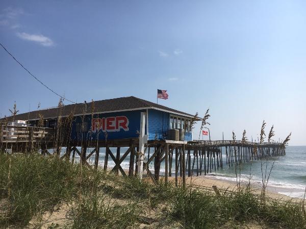 Avon Fishing Pier Blue Building with fishing pier extending into ocean on beach front.