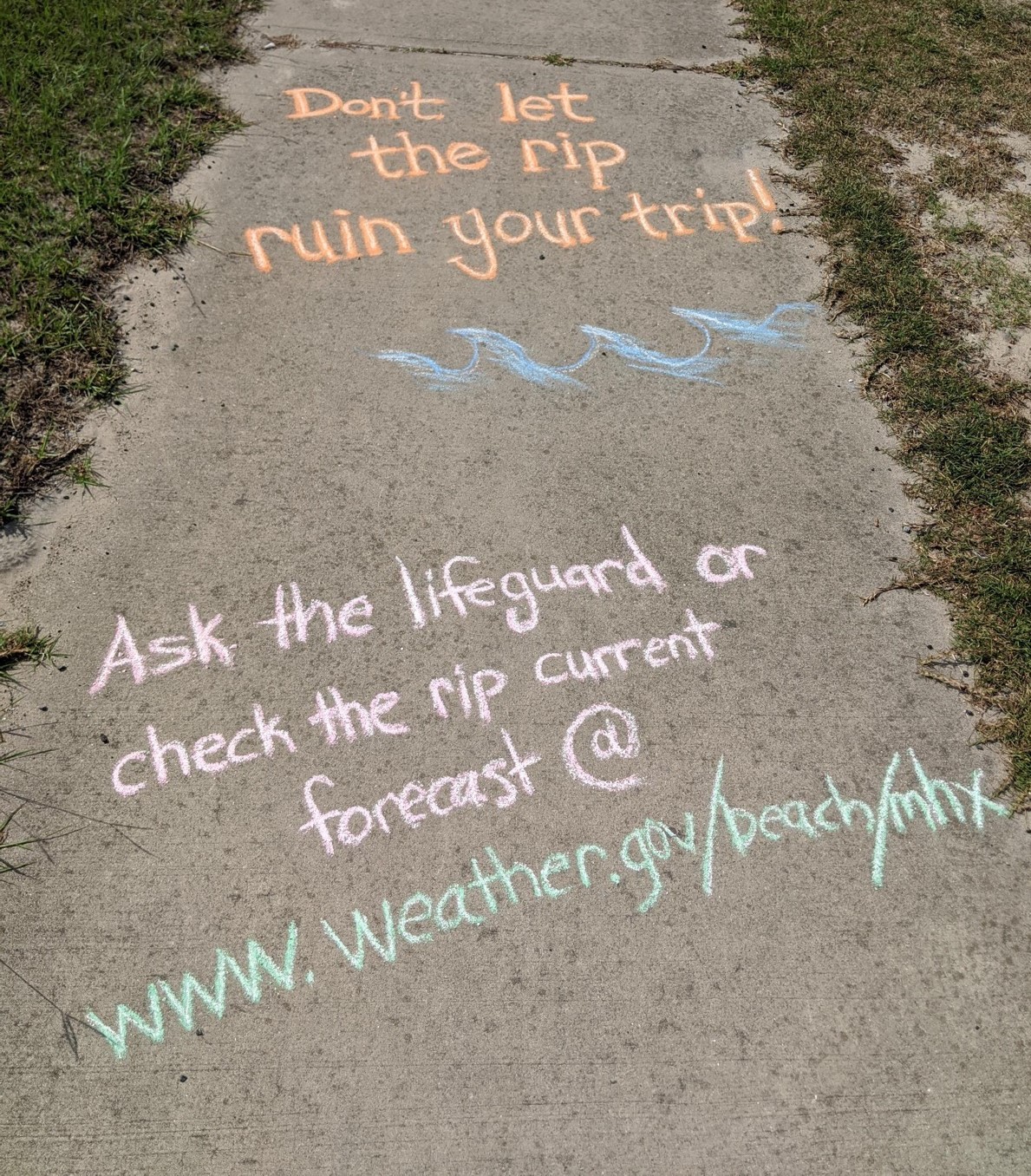 Two ocean safety messages in chalk on a sidewalk.