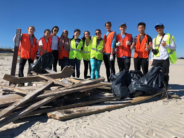 Eleven students standing near piles of trash that was picked up from the beach near the Bodie Island Lighthouse.