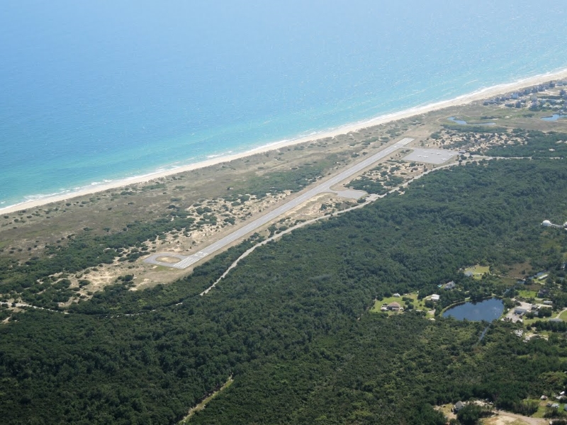 Aerial view of the Billy Mitchell Airport and surrounding forest areas and nearby ocean.