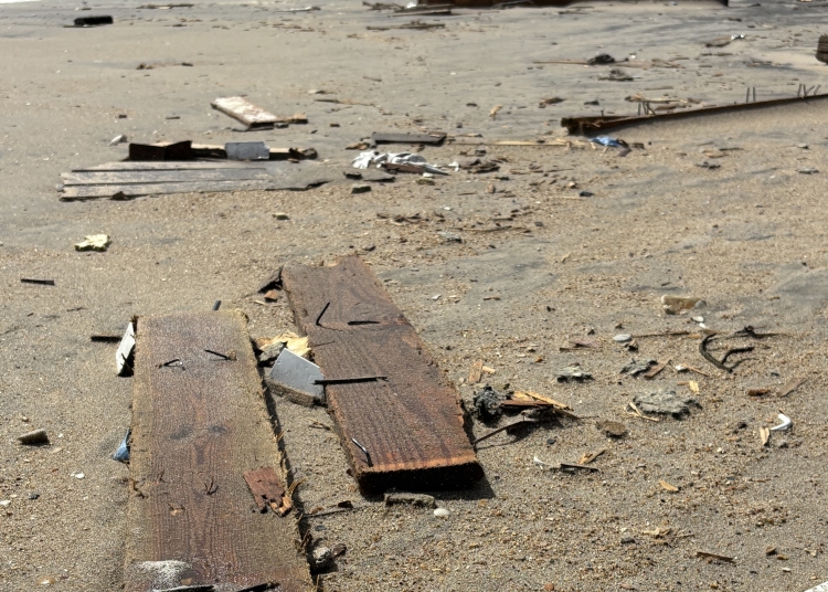 Wooden debris with nails sticking out of them on the beach.