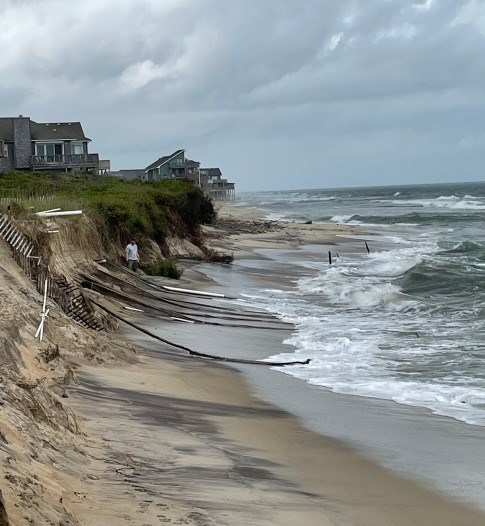 Photo showing significant beach erosion and exposed white PVC pipes.