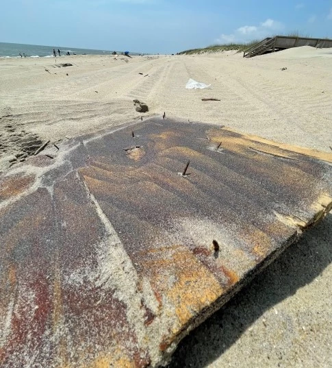 Wood with exposed nails on beach Large slab of wood containing exposed nails.