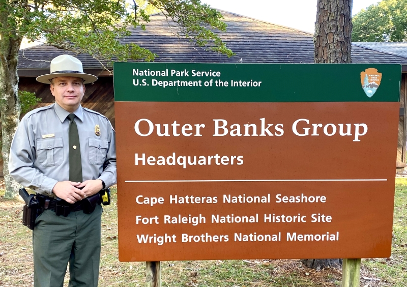 Chief Ranger Mike Henry at Fort Raleigh National Historic Site. Photo of park ranger standing next to sign that reads "Outer Banks Group Headquarters"