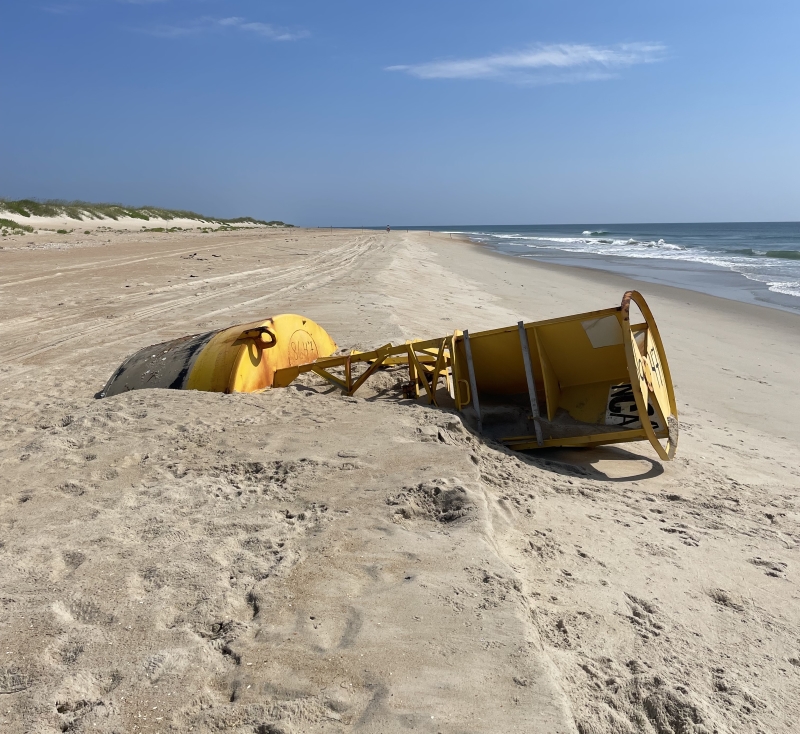 Partially buried Coast Guard buoy located north of Ramp 34. Image of a large sea buoy partially buried in a beach.