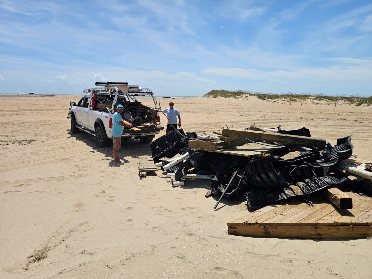 Collection of debris cleaned up by NCBBA following Hurricane Erin. Two people in blue shirts stand next to white pickup truck and collected debris associated with a house.