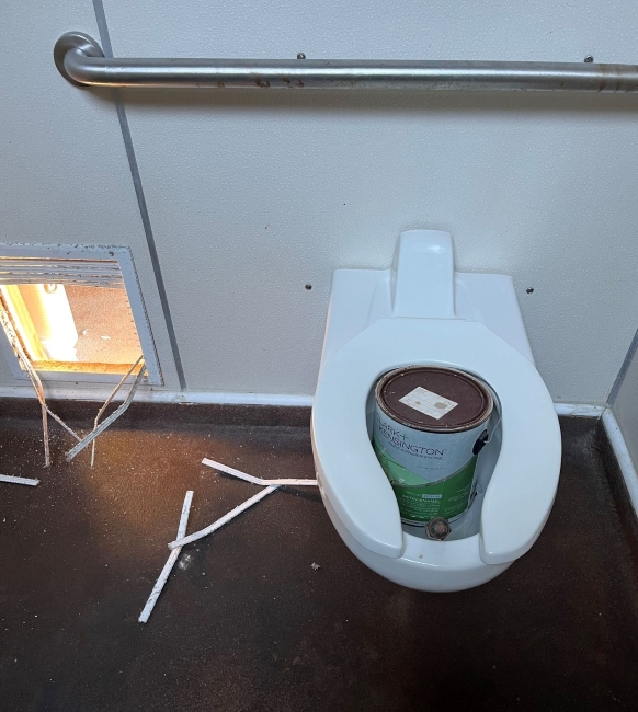 White toilet containing a paint can next to a broken vent.