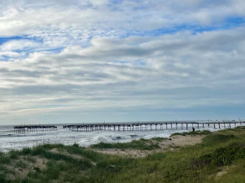 An image of a damaged pier in the ocean. There is a missing section near the end of the pier.