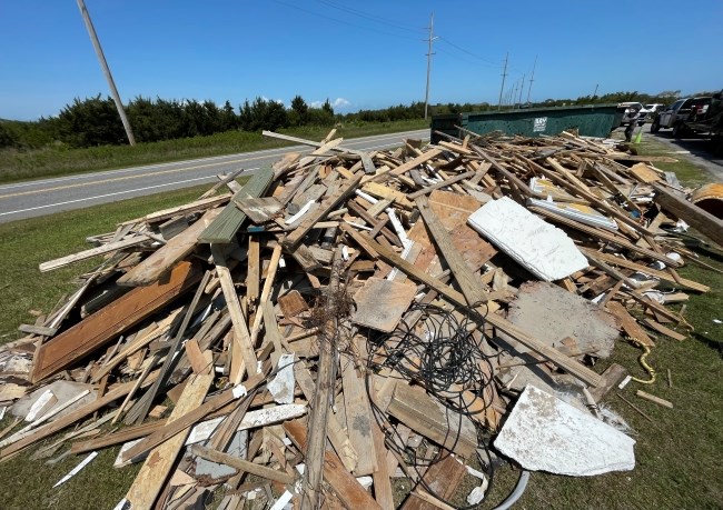 Debris staged for removal at ORV Ramp 23. Large pile of collected beach debris near highway.