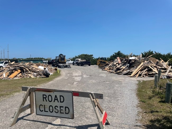 "Road Closed" sign in front of large piles of collected beach debris.