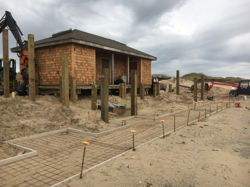 Contractors and construction vehicles take part in a project to replace sidewalk, ramps, and exterior of restroom facility.