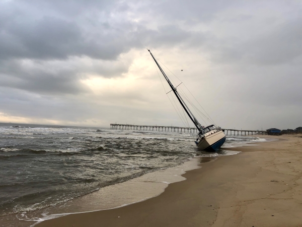 A sailboat sits grounded with a fishing pier in background.