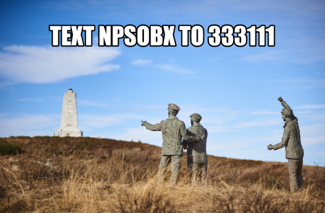 Text alert advertisement featuring bronze sculpture of three individuals with monument in background.