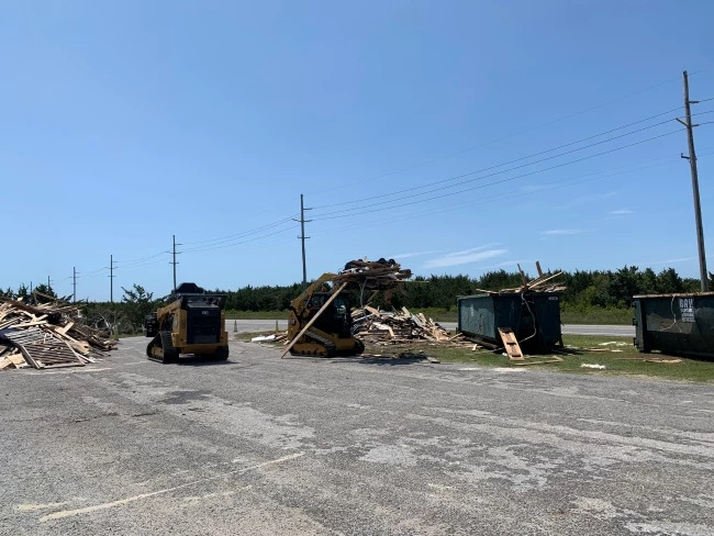 NPS staff use heavy equipment to load dumpsters with beach debris at ORV Ramp 23. Two pieces of heavy equipment work to load beach debris into green dumpsters.