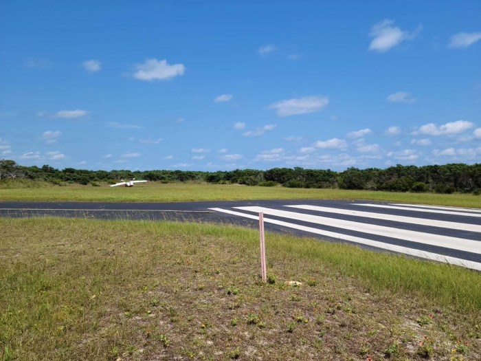 Photo of overturned airplane at end of runway in grass.