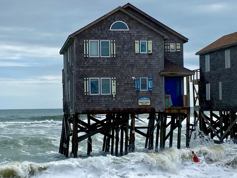 Photo of 23039 G A Kohler Court a couple hours before its collapse. Photo of leaning house on pilings in the ocean.