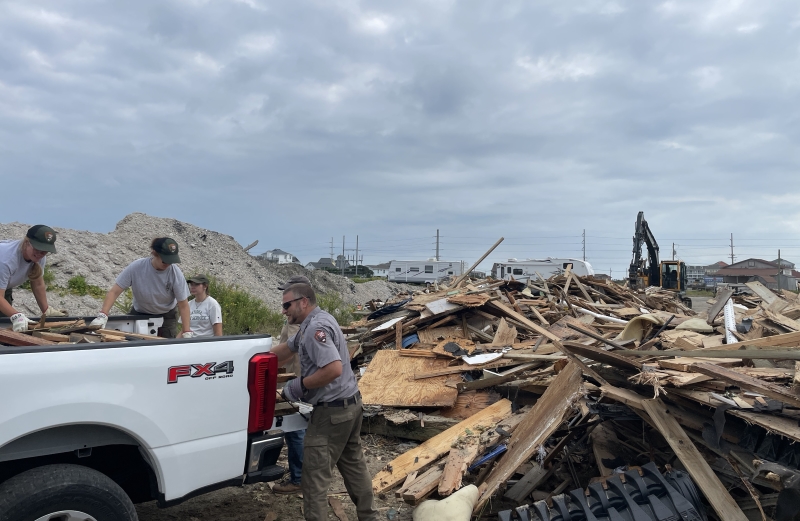 Photo of NPS employees unloading house collapse debris 09-25-20241 Four people in uniform offload a truck full of wooden debris.