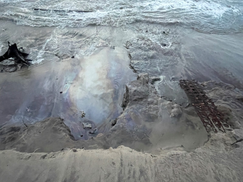 Photo showing rainbow colors associated with petroleum sheen on beach.