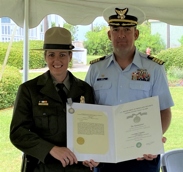 Park Ranger holds silver lifesaving medal certificate while standing next to Coast Guard officer.