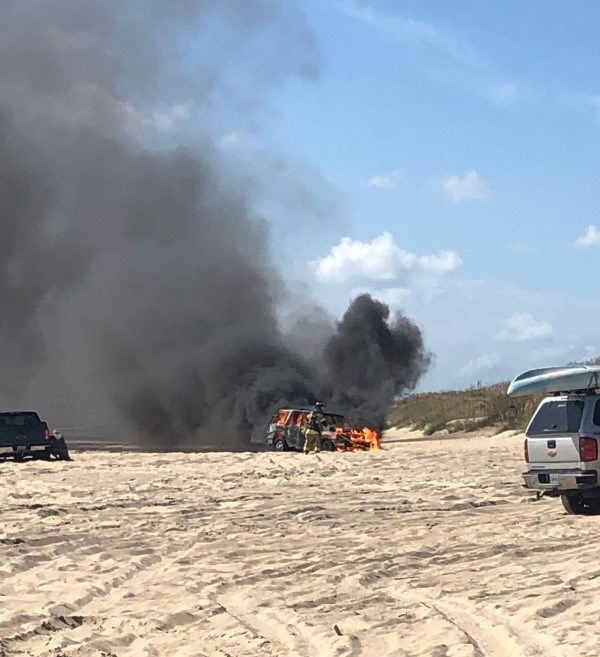 A firefighter works to put out vehicle fire on beach.