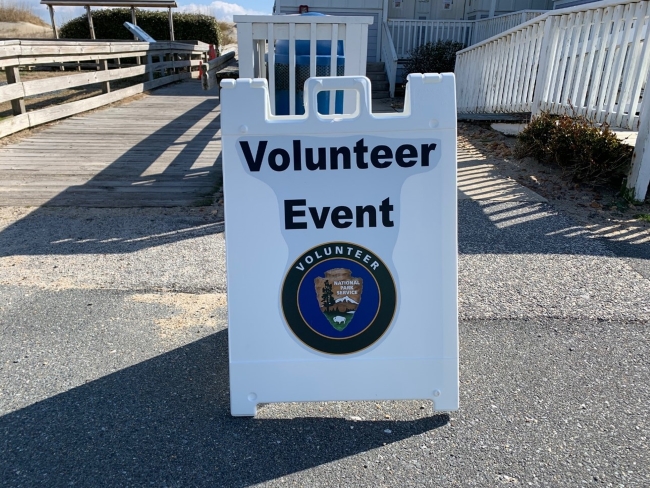 White sign that says "Volunteer Event" with volunteer/NPS arrowhead logo.
