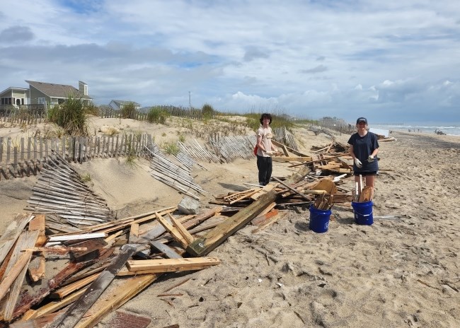 Two young beach cleanup volunteers stand near piles of collected debris.