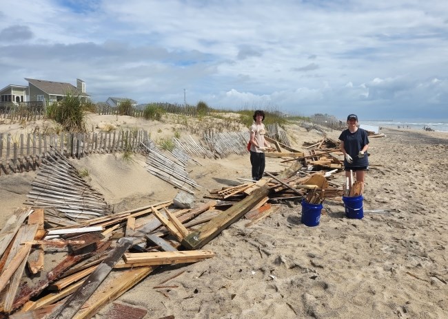 Volunteers at beach cleanup 05-14-2022 Two young beach cleanup volunteers stand near piles of collected debris.